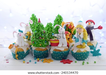 Festive cupcakes with sugar figures on a bright lights background. Three rabbits  and Snow Maiden decorating the Christmas tree.