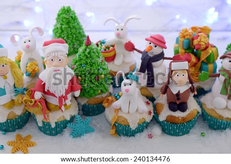 Festive cupcakes decorated with sugar figures of a kid in a fur hat Santa Claus and a rabbit selective cropping.