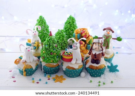 Festive cupcakes with sugar figures on a bright lights background horizontal format. Three rabbits  and a kid in a fur hat decorating the Christmas tree.