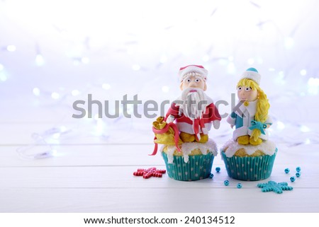 Cupcakes with sugar Santa Claus and Snow Maiden  on the Christmas lights background closeup.