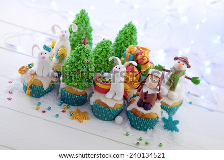 Festive cupcakes with sugar figures on a bright lights background diagonal crop. Three rabbits  and a kid in a fur hat decorating the Christmas tree.