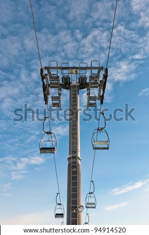 Top part of ski-lift support and few chairs on ropes