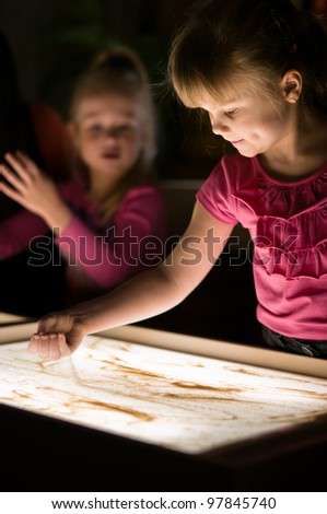 Girl pours sand on table from her hand in classroom with friends