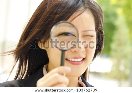Asian business woman with magnifying glass to the eye