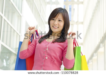 Happy young Asian shopper holding shopping bag in shopping mall