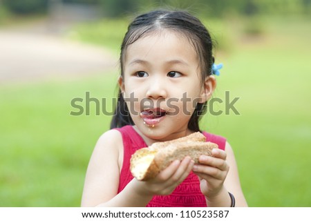 Little Asian girl eats a sandwich and licking lips on fresh air