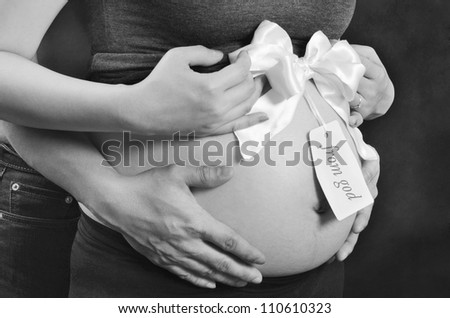 Pregnant woman and husband hand on stomach with ribbon and tag