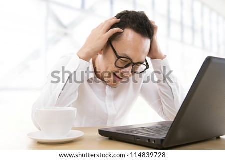 Depressed mid adult Asian business man scratching his head at office
