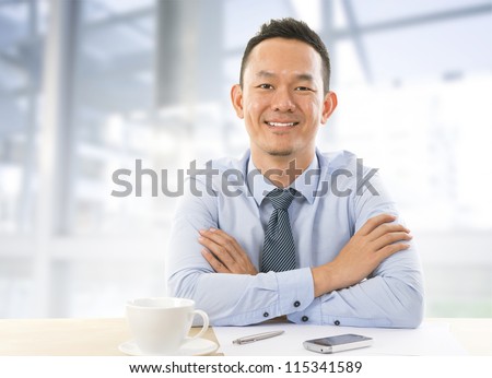 Mid aged Asian Businessman sitting at table in office