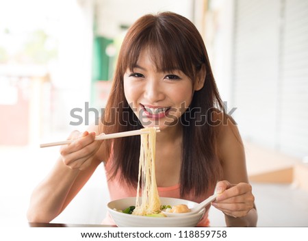Portrait of happy smiling young Asian woman eating Asian noodles