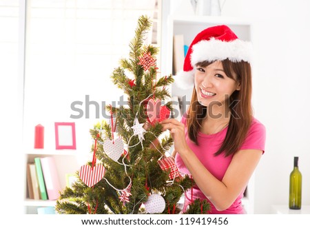 Beautiful Asian woman decorating Christmas tree in her house