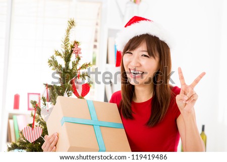 Excited Asian woman getting her Christmas present, showing peace hand sign, indoor/inside her home.