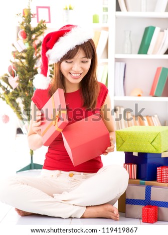 Beautiful Asian female peeking inside Christmas gift, indoor / inside house