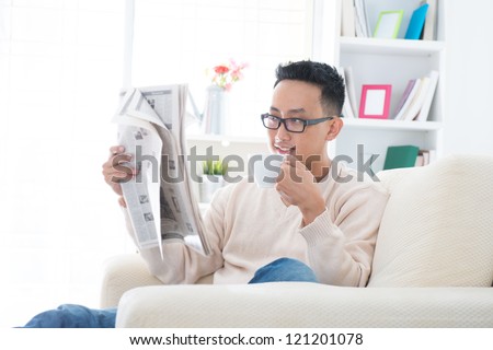 Southeast Asian male drinking coffee while reading news paper sitting on sofa at home, indoor lifestyle