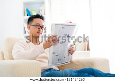 Southeast Asian male reading news paper sitting on sofa at home, indoor lifestyle