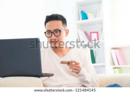 Southeast Asian male holding credit card online shopping at home