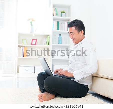 Asian man browsing internet at home, sitting on floor.