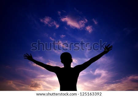 Silhouette or backlit of Asian man open arms raised towards sky on sunset