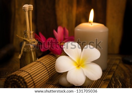 Low light spa setting indoor with candle, frangipani and aroma set.