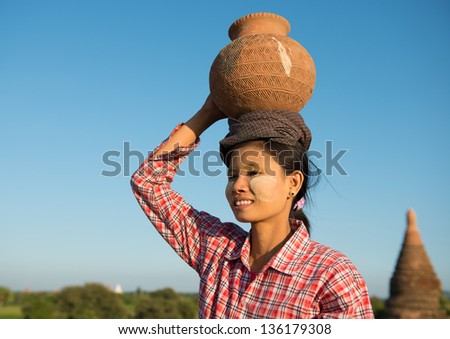 Portrait of Asian traditional female farmer carrying clay pot on head going back home, Bagan, Myanmar