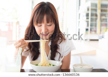 Eating Noodles At Restaurant. Young Asian Girl Eating Ramen Noodles Using Chopsticks.