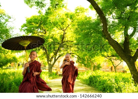 Two little Buddhist monks running outdoors under shade of green tree outside monastery Myanmar Two little Buddhist monks running outdoors under shade of green tree outside monastery Myanmar