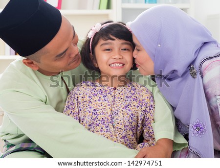 Muslim parents kissing child. Southeast Asian Malay family lifestyle. Happy smiling father mother and daughter.