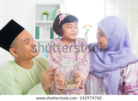Islamic banking concept. Southeast Asian Malay family saving money at home. Muslim father, mother and daughter living lifestyle.