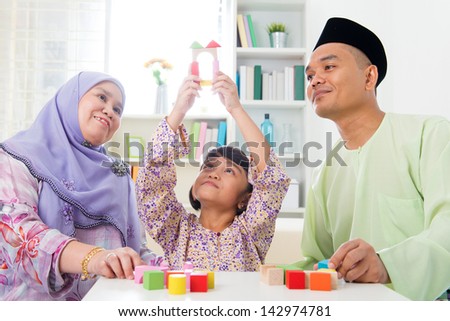 Malay family at home. Muslim girl building a wooden toy house. Southeast Asian parents and child living lifestyle.