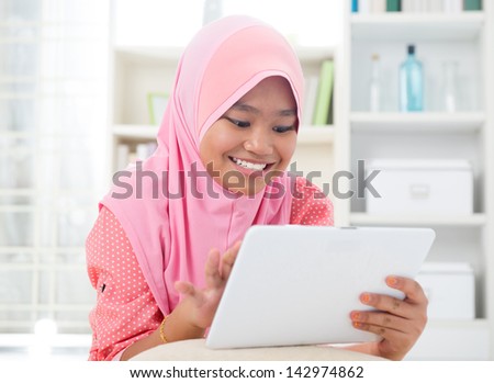 Asian teen using tablet pc computer. Southeast Asian teenager at home. Muslim teenage girl living lifestyle.