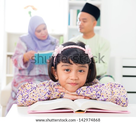 Muslim girl reading book. Malay family at home. Southeast Asian parents and child living lifestyle.