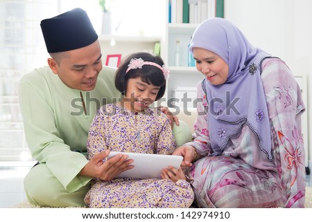 Southeast Asian family using tablet pc computer at home. Muslim family living lifestyle. Happy smiling Malay parents and child.