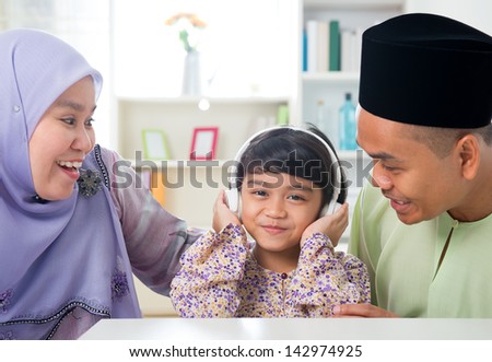 Muslim girl listening to music at home. Southeast Asian family living lifestyle. Happy smiling Malay parents and child.