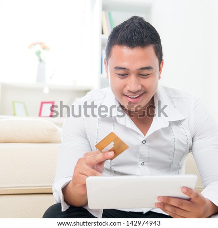 Internet shopping man online with tablet pc and credit card. Internet shopper buying things on the internet. Handsome multicultural Asian model. model happy