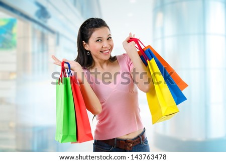Happy Asian shopping woman smiling holding many shopping bags at the mall. Casual Asian shopper girl standing in department store. Beautiful mixed race Caucasian Southeast Asian woman model.