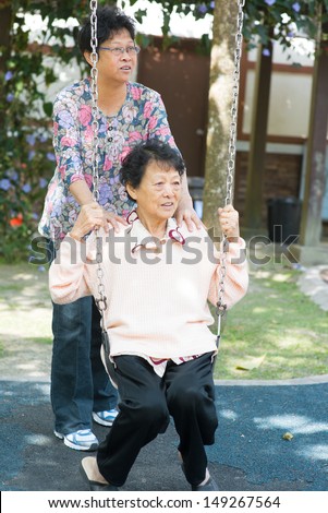 80s Asian old mother and 60s senior daughter playing swing at outdoor garden park.