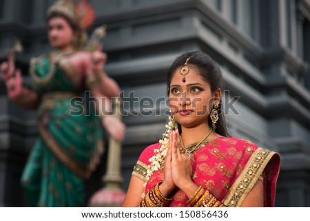 Beautiful young Indian woman in traditional sari dress praying in a hindu temple.
