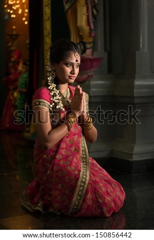 Young Indian woman in traditional sari dress praying in a hindu temple.