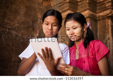 Portrait of two beautiful young traditional Myanmar girl using digital tablet pc together.