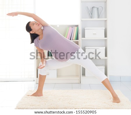 Prenatal health concept. Full length healthy 8 months pregnant calm Asian woman meditating or doing yoga exercise at home. Relaxation yoga side stretching pose.