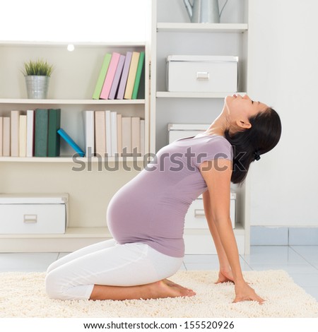 Pregnancy yoga meditation. Full length healthy 8 months pregnant calm Asian woman meditating or doing yoga exercise at home. Relaxation yoga sitting back bending positions.