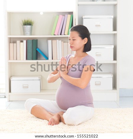 Pregnancy yoga meditation. Full length healthy 8 months pregnant calm Asian woman meditating or doing yoga exercise at home. Relaxation yoga positions.