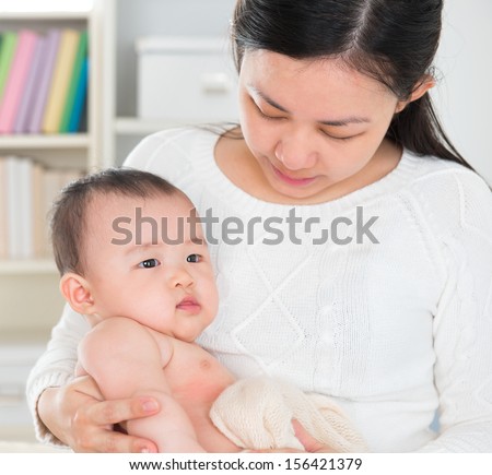 Beautiful Asian mother pampering six months old baby girl at home.
