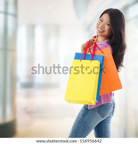 Happy Asian shopping woman smiling holding many shopping bags at the mall. Casual Asian shopper girl standing in department store. Beautiful mixed race Southeast Asian woman model.