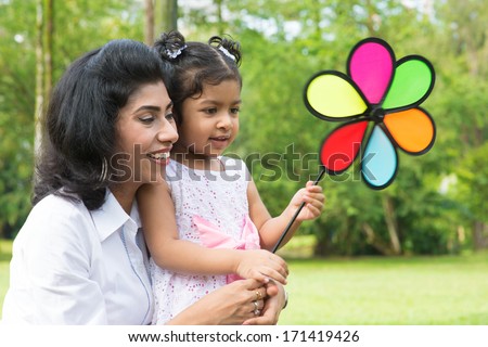 Happy Indian family outdoor activity. Candid portrait of parent and child playing windmill at garden park.