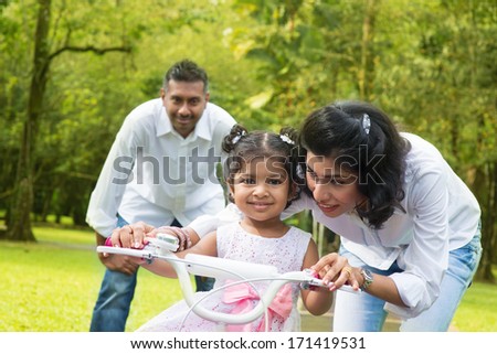 Indian Family Outdoor Activity. Asian Parent Teaching Child To Ride A Bike At The Park In The Morning.