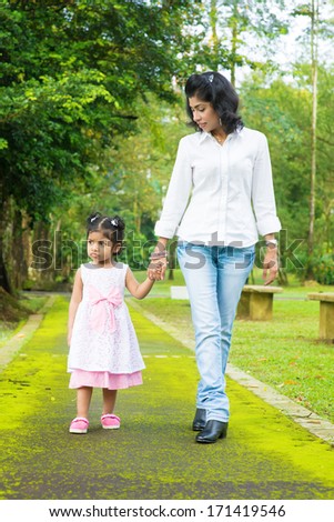Indian family walking on garden path. Mother and daughter holding hands at outdoor park.
