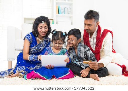 Indian Asian family using tablet pc computer online shopping with credit card at home. India family living lifestyle. Happy smiling parents and children.