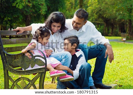 Happy Indian family at outdoor park. Candid portrait of parents and children having fun at garden park.