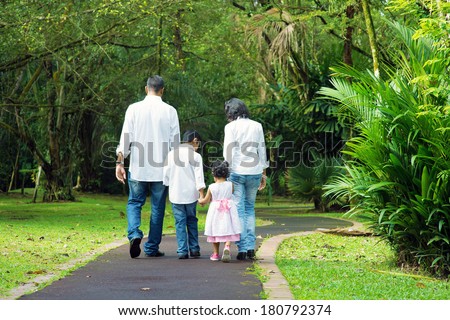 Indian family at outdoor. Rear view of parents and children walking on garden path. Exploring nature, leisure lifestyle.